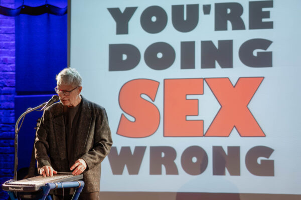 A man standing in front of a screen that says " you 're doing sex wrong ".